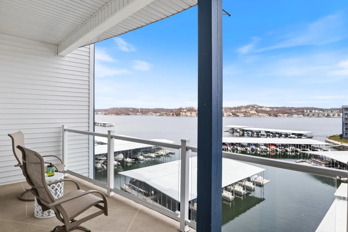 A tranquil balcony scene overlooking a marina with seating arranged to enjoy sweeping lake views. The peaceful water is dotted with boats and the marina infrastructure, suggesting a vibrant, active boating community. The vantage point emphasizes private relaxation while maintaining connection to the lake.