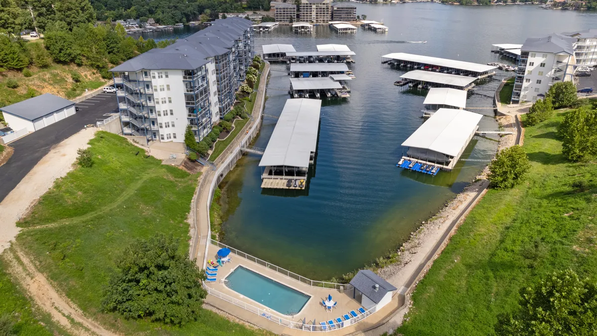 A broad exterior view showing a marina with boats docked, a swimming pool, landscaped grounds, and residential buildings. People are seen boating, swimming, and relaxing by the pool, highlighting the community’s active, social vibe and the seamless connection between land and water recreation.
