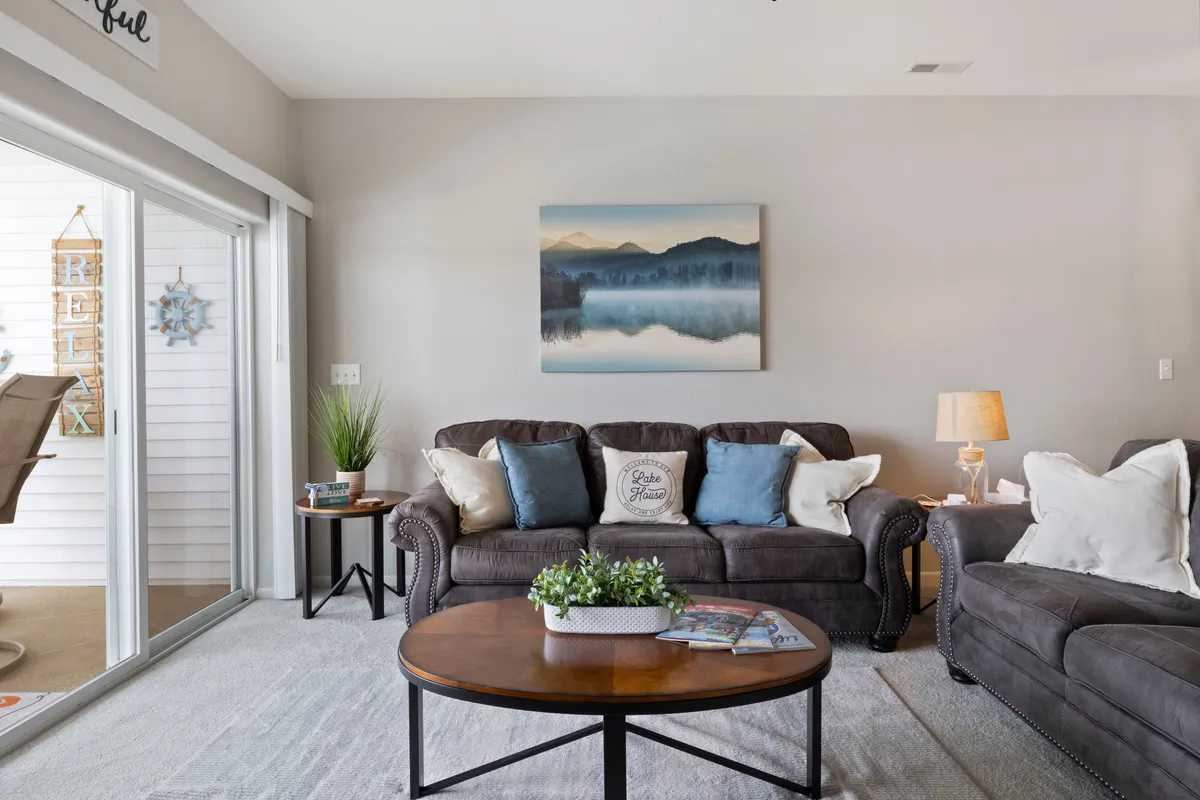 A calm and comfortable living area with a sofa adorned with blue cushions, a round coffee table, and mountain-themed wall art. The arrangement epitomizes a relaxing, safe environment perfect for unwinding after a day out, echoing the feeling of peace of mind emphasized in the section.