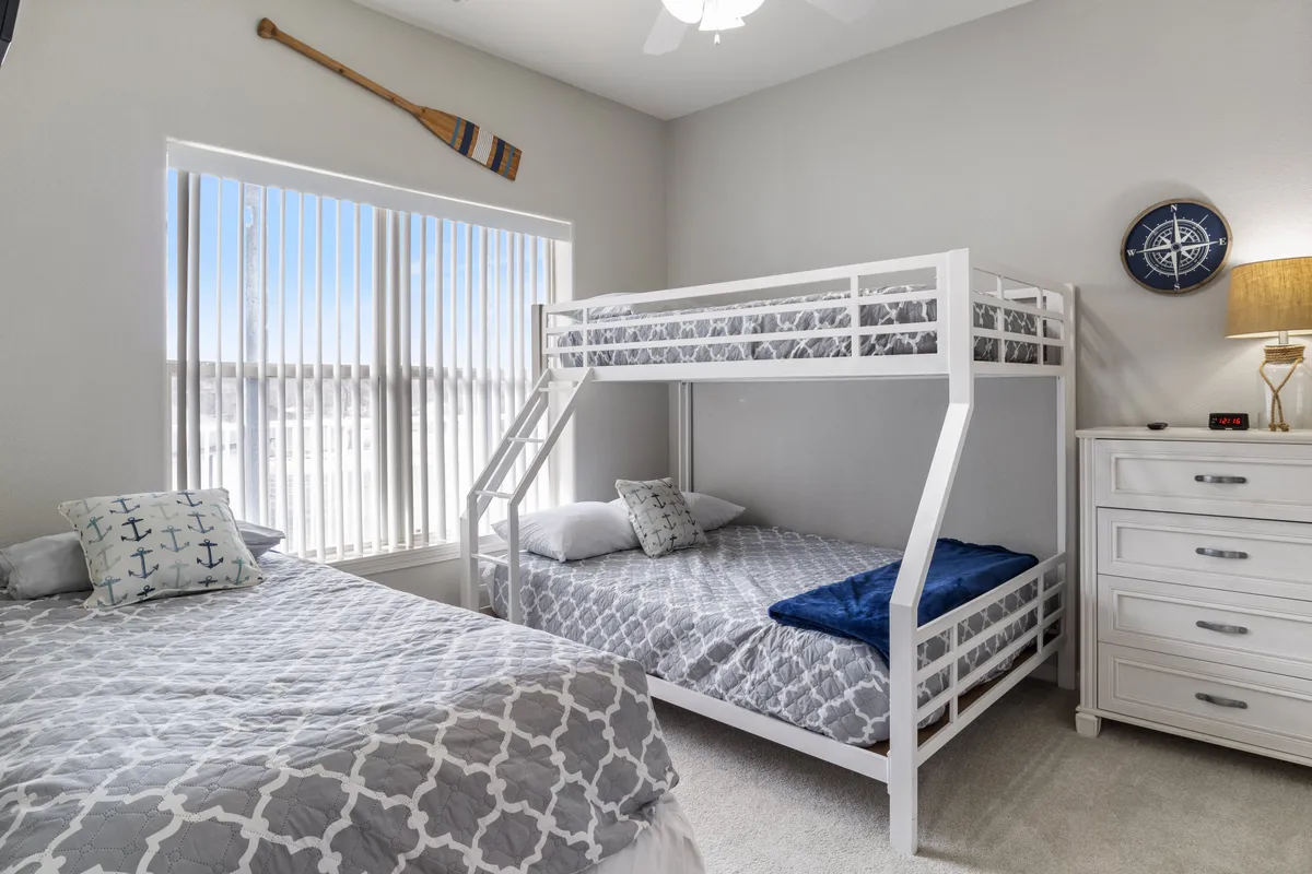 A cozy and playful bedroom featuring a bunk bed and a double bed, accented with a decorative oar and compass wall decor. The dresser and comfortable bedding create a welcoming space ideal for families or groups, encouraging both restful sleep and bonding moments.