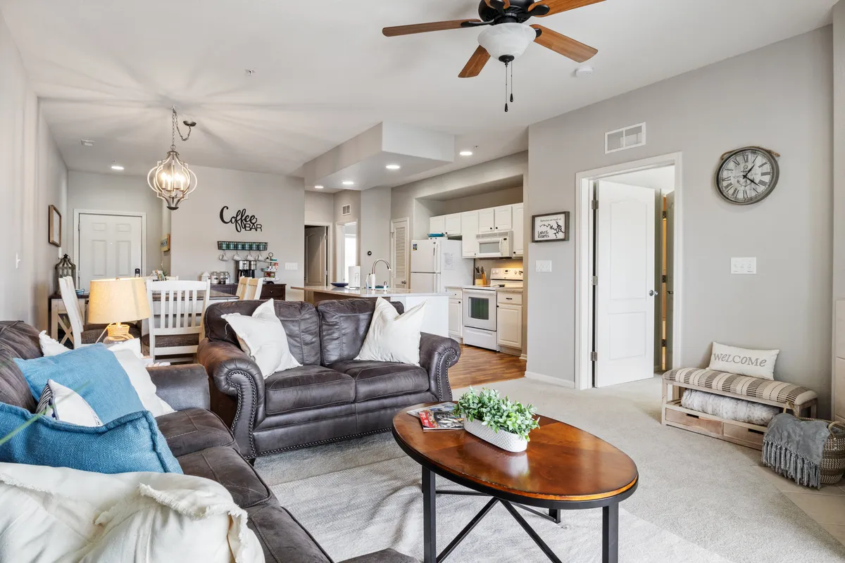 This image captures a welcoming entryway and living space featuring a leather sofa, coffee table, kitchen area, decorative clock, and a prominent welcome sign. The open layout subtly references the point of arrival and seamless guest access, as well as the inviting, well-managed atmosphere.
