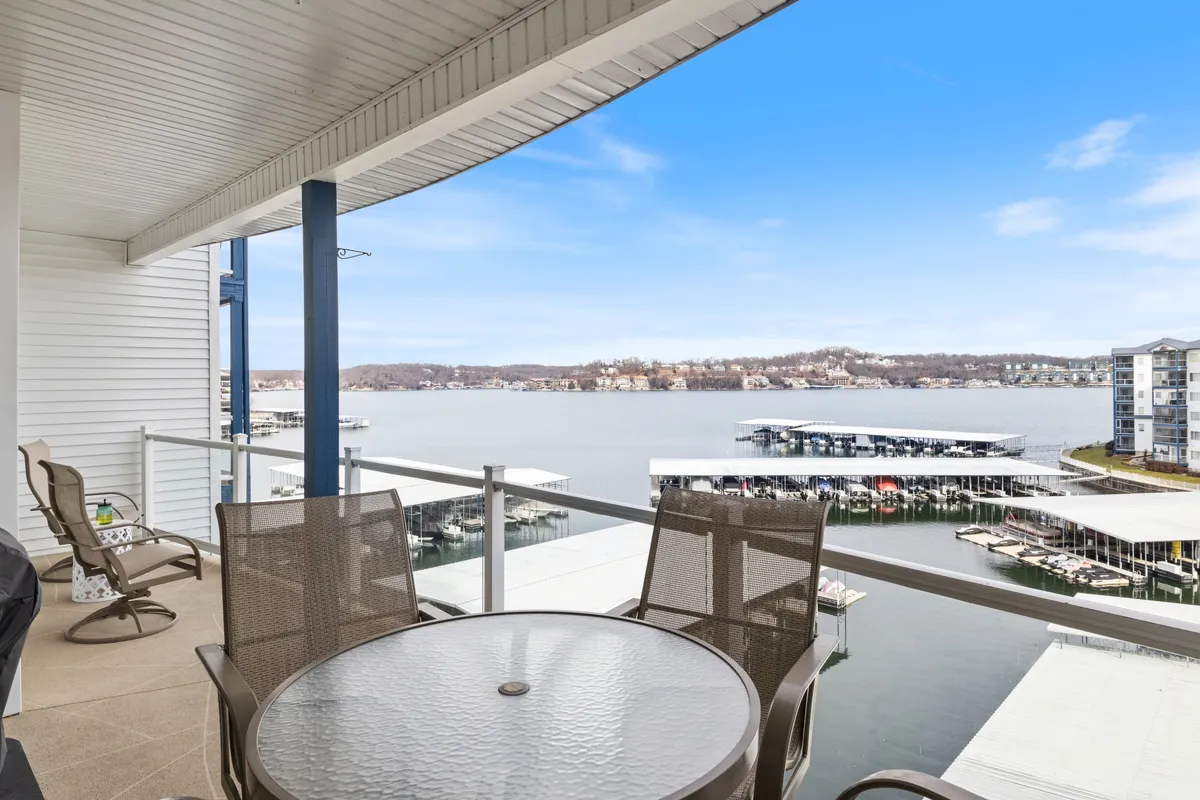 A tranquil exterior shot showing a balcony with seating that overlooks the lake, boat docks, and calm water. The scene evokes relaxation, outdoor enjoyment, and the appeal of lakeside living.