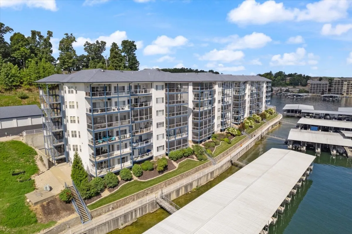 A modern apartment complex framed by lush greenery and featuring a lakeside dock stretching into the water. The peaceful setting invites couples to explore or relax by the water, with boating and lakeside walks on offer.