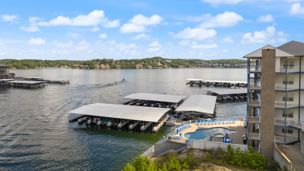A panoramic view of the lake, boat docks, a sparkling swimming pool, and surrounding greenery. The image also captures nearby buildings, tying together water, recreation, and residential elements in a single frame.