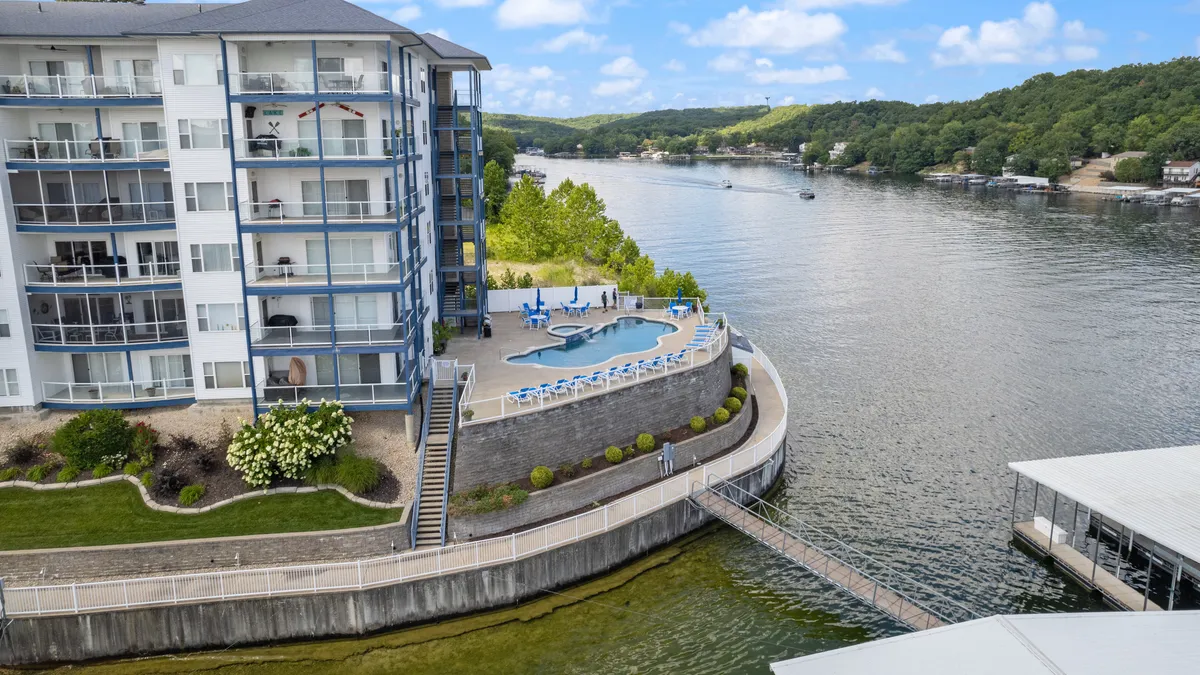 An inviting pool scene looking out over the lake, with outdoor seating and landscaped gardens adding to the resort atmosphere. The water is calm and reflective, and the pool area is set up for both relaxation and social gatherings. The photo exudes tranquility and showcases sunset views, tying into the lakeside allure.